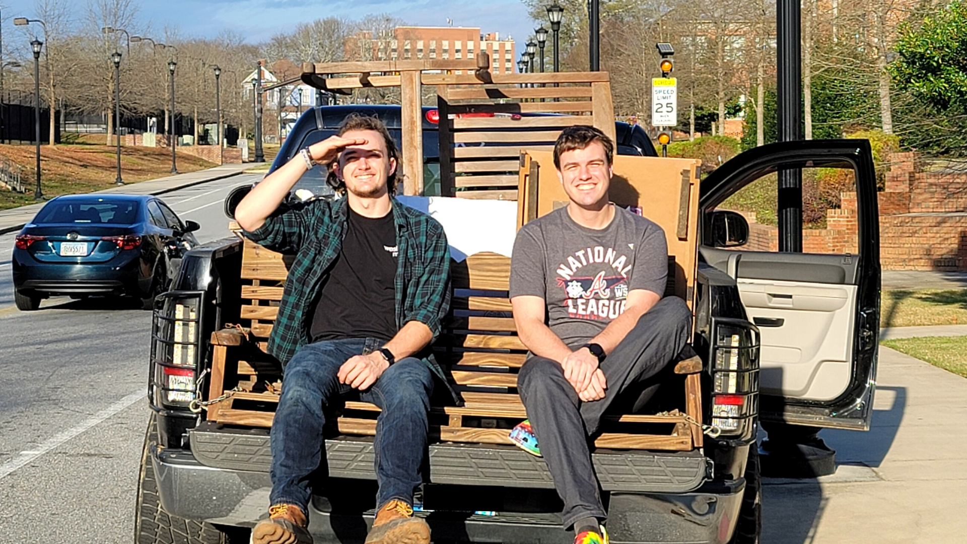 Two guys sit on the back of a truck.